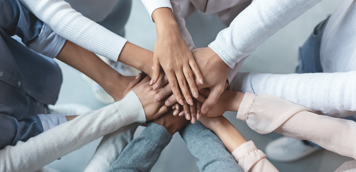 multiracial group of friends demonstrating cooperation and empowerment with putting their hands together on top of each other
